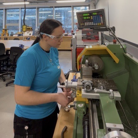Bethany in the workshop, wearing safety goggles, using a lathe.