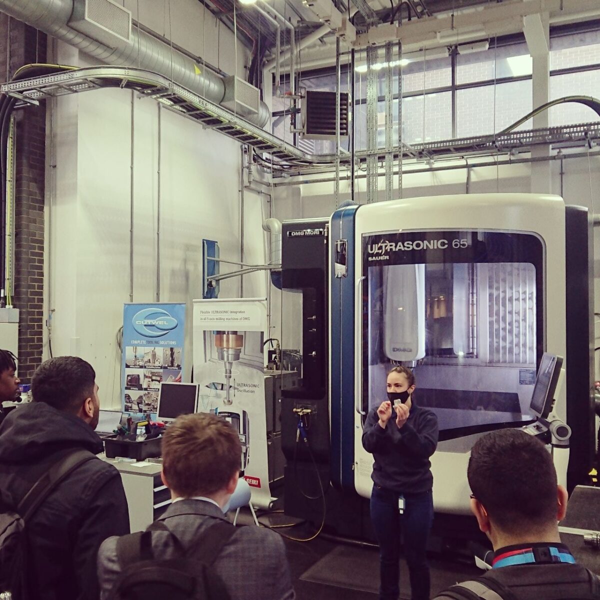 Bethany Haynes standing in front of a design machine, talking to a group of students.