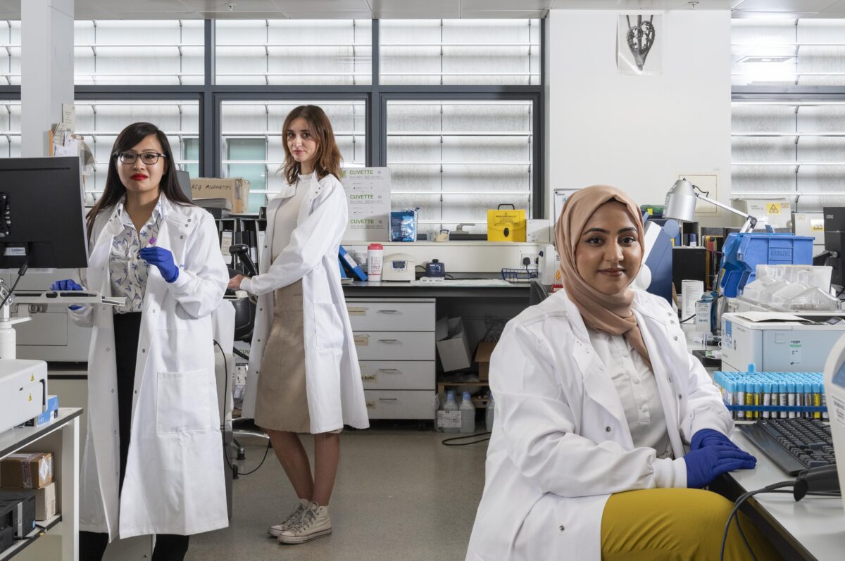 Three technicians wearing lab coats in a healthcare laboratory.