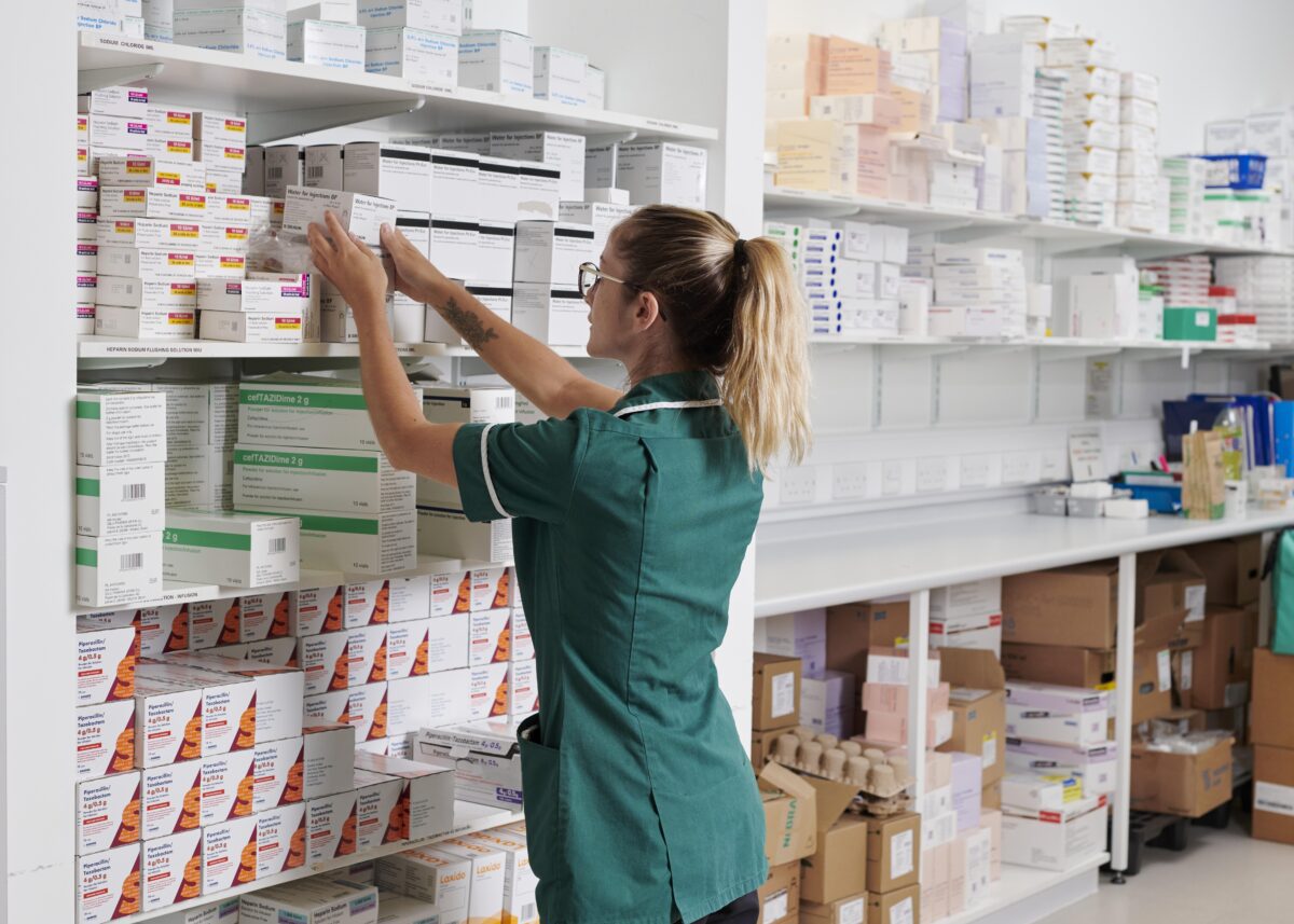 A pharmacy technician organising shelves of medicine boxes.