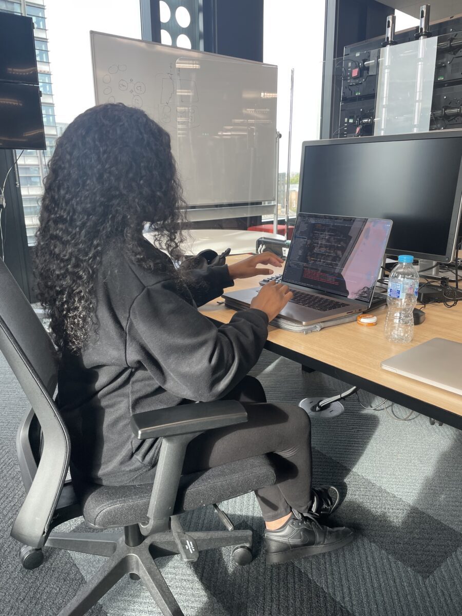 Esther at her desk, working on her laptop and screen.