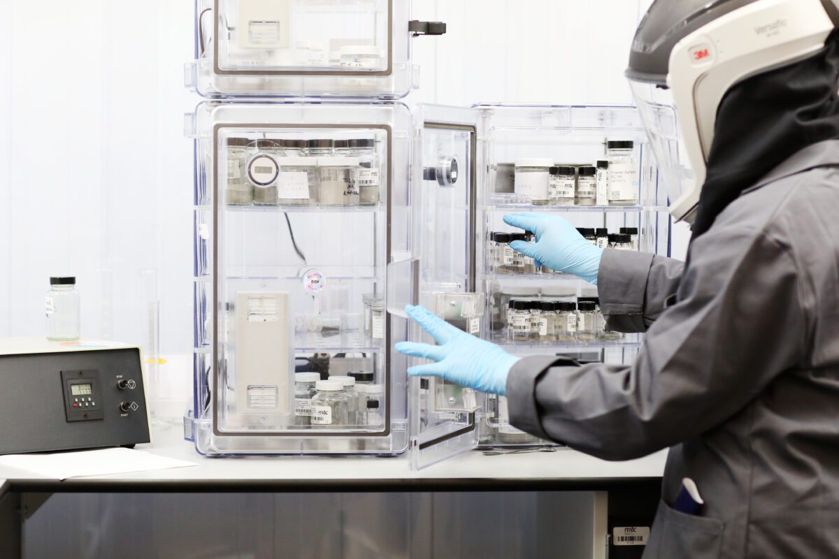 An engineering manufacturing technician working in lab, wearing a protective visor and gloves.