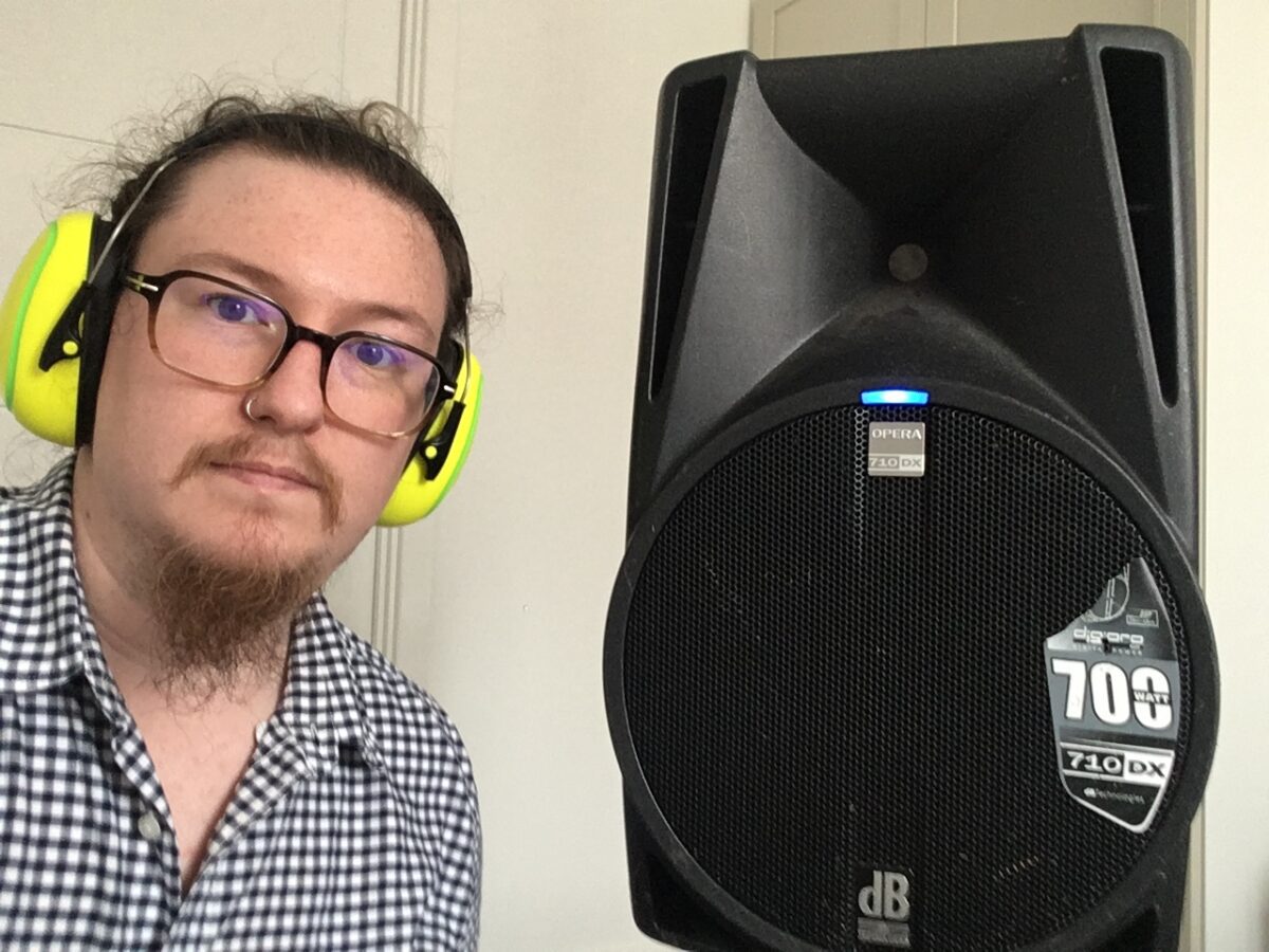 Baden Fitzmaurice standing next to a large speaker, wearing ear defenders.
