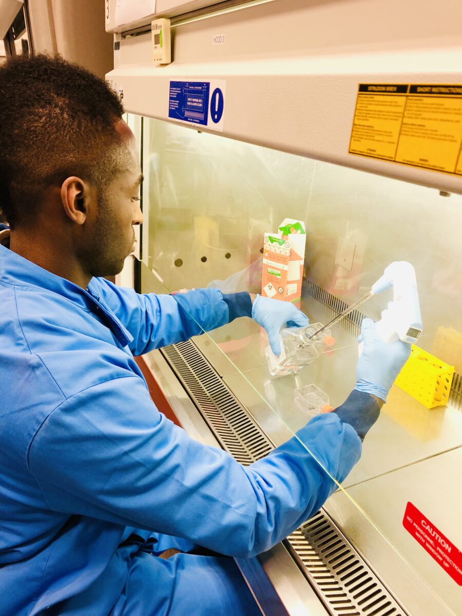 Nana preparing a sample under a fume hood, wearing a lab coat and protective gloves.