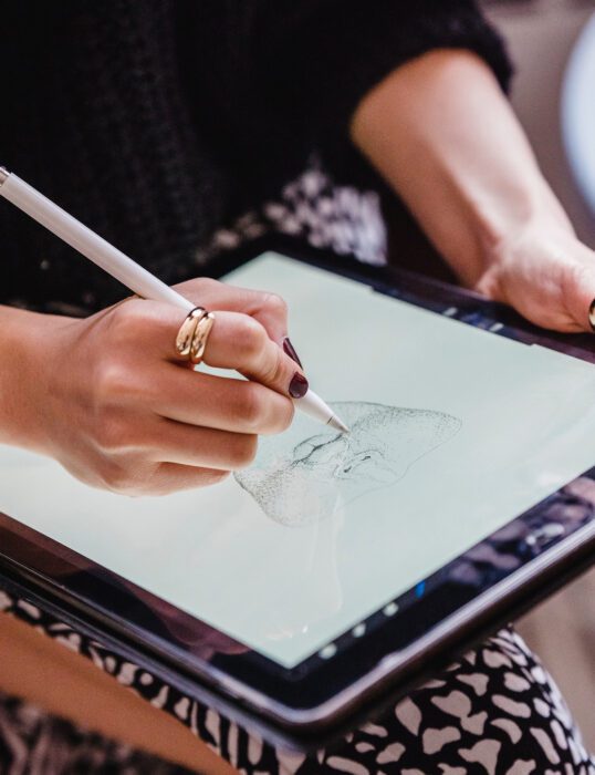 A woman's hand drawing a man's face on an iPad.