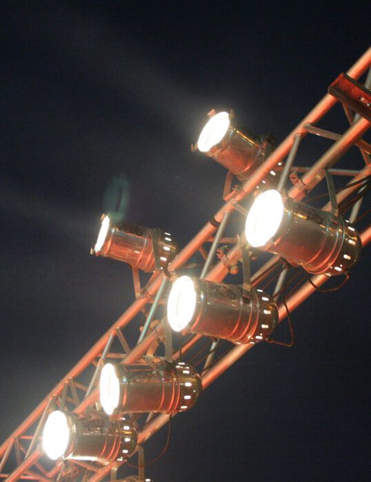 An overhead lighting rig, with multiple bright floodlights shining.