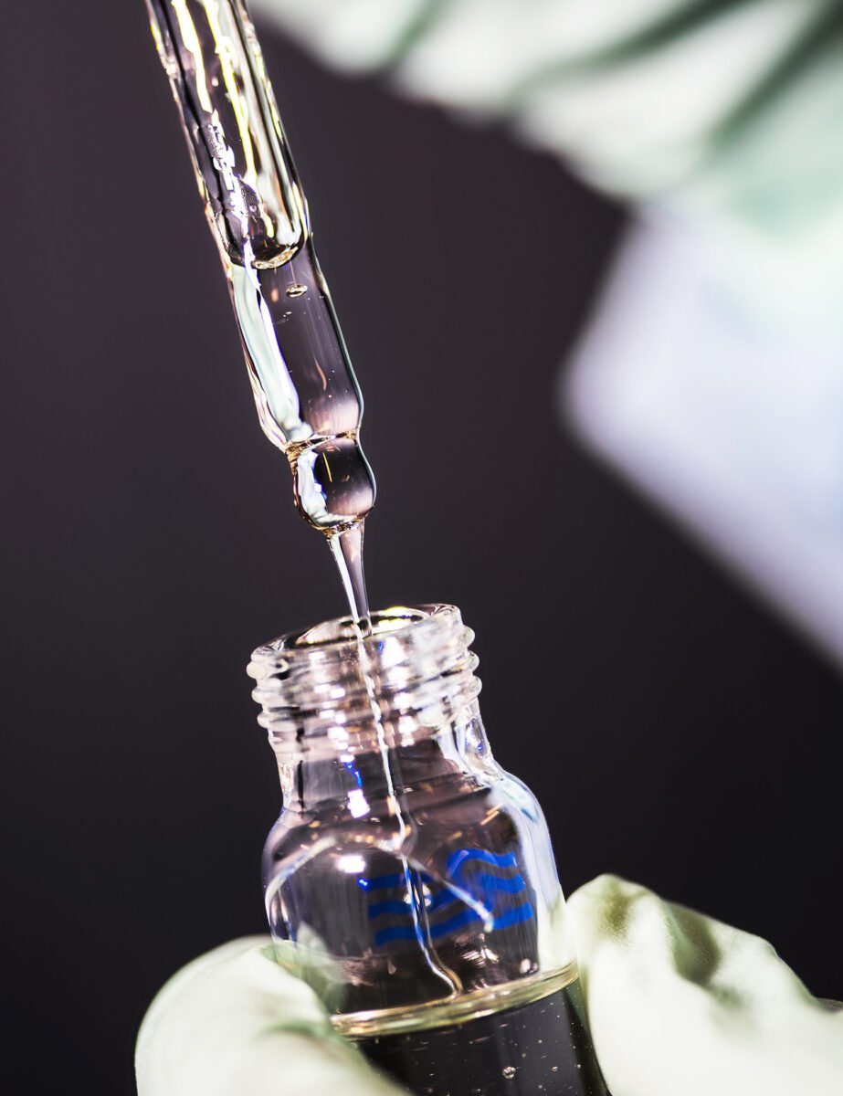 A technician wearing gloves pulling a pipette out of a glass bottle of viscous liquid.
