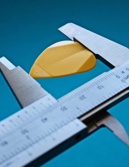 A guitar pick being held by the prongs of a calliper, it's length being accurately measured.
