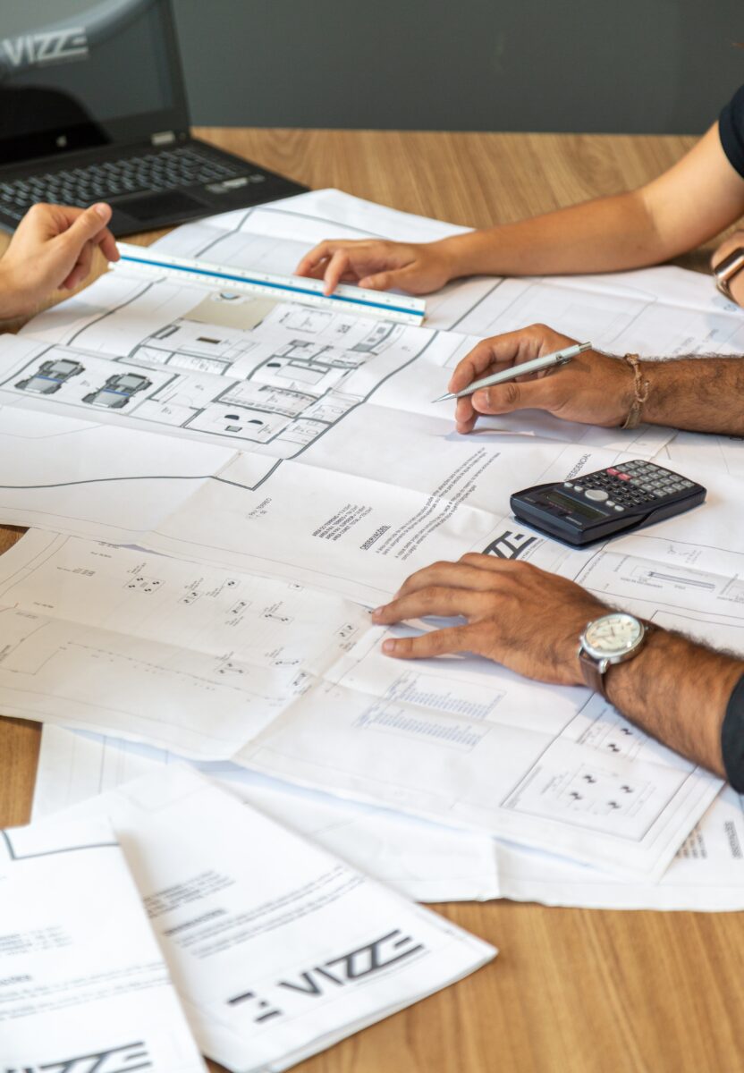 Architectural technicians discussing and annotating printed architectural drawings.