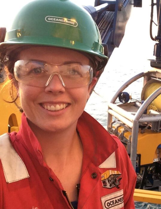 Charlotte Cunningham at sea, wearing a hard hat and safety goggles, about to launch her remotely operated vehicle overboard.