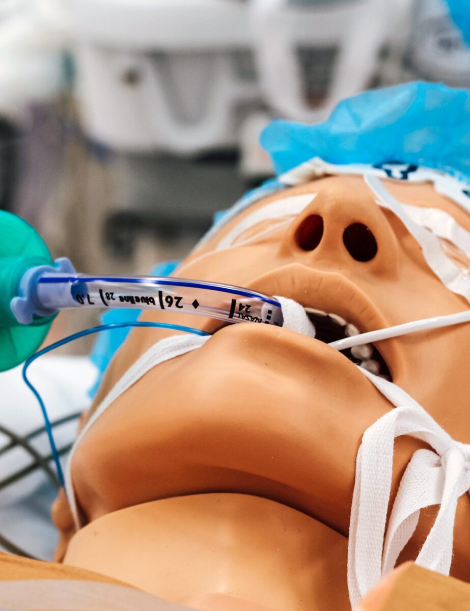 A medical dummy lying down with a manual resuscitator in its mouth.