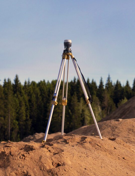 Surveying equipment on a tripod, overlooking a forest.