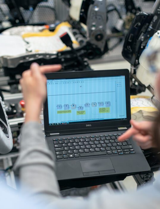 Technician using a laptop to test software running in a car manufacturing plant.