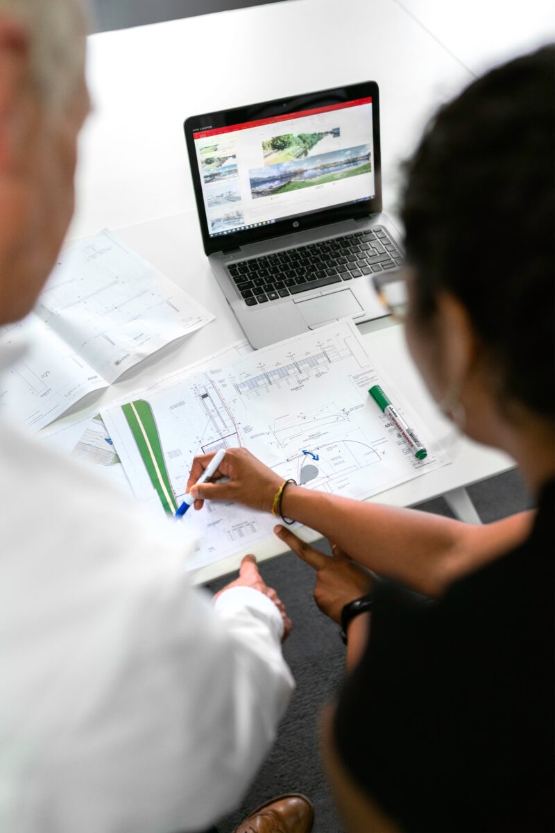 A man and woman discussing and annotating engineering drawings.