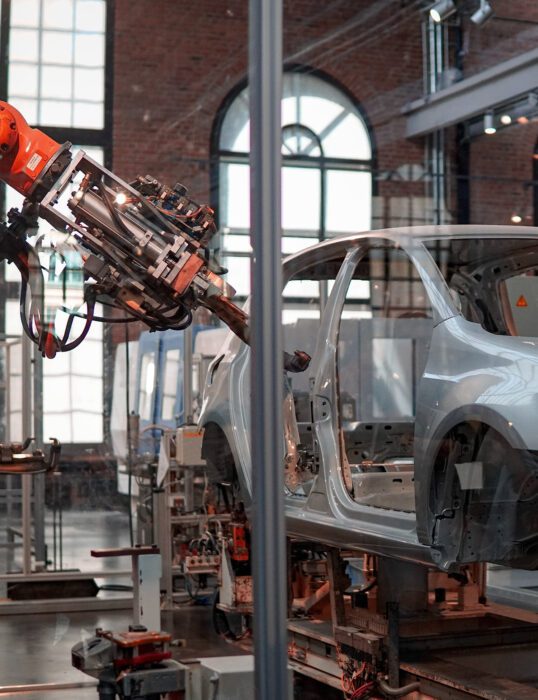 Empty frame of a car being painted by a robot arm.