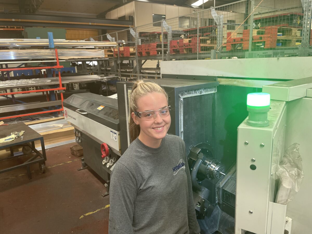 Holly working on industrial machinery, wearing safety goggles.