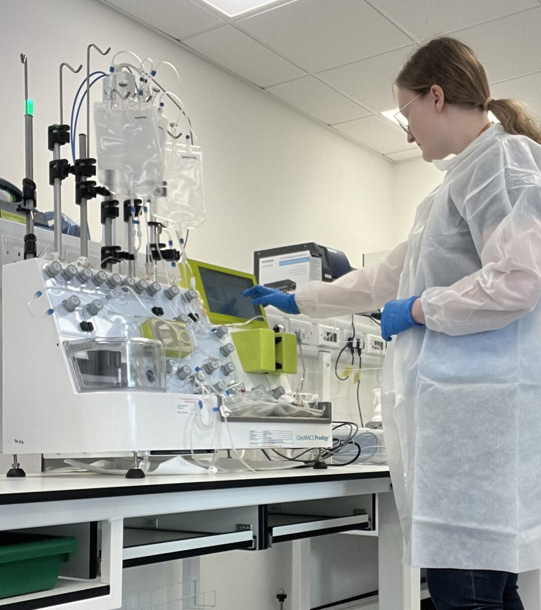 Lara operating equipment in the lab, wearing a lab coat and protective gloves.