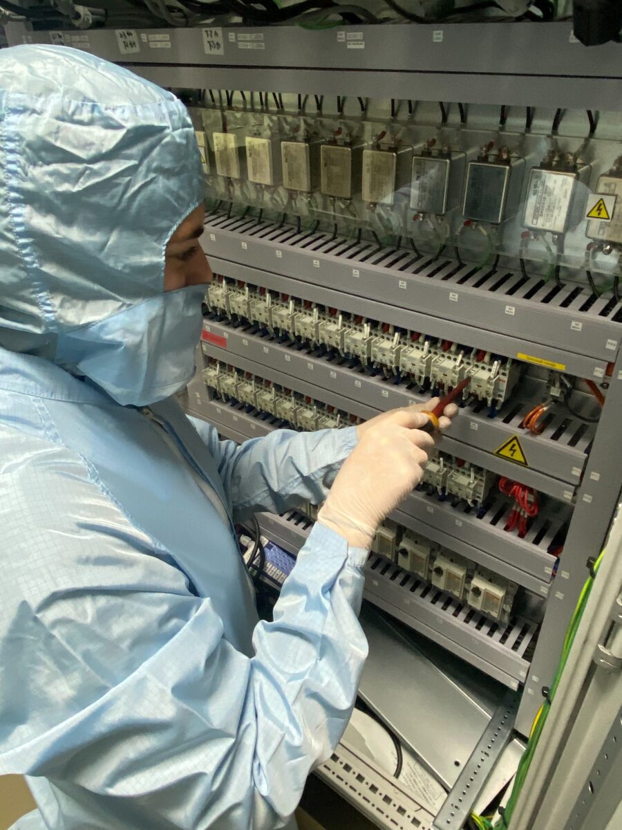 Molly in a full clean suit, using a screwdriver to work on electrical equipment.