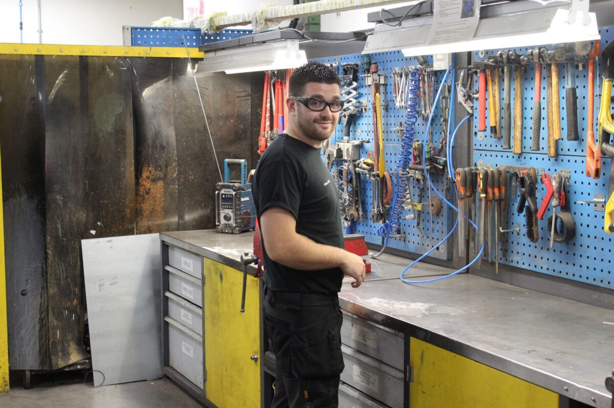 Connor Johnson in the workshop with tools hanging on the wall, wearing safety goggles.