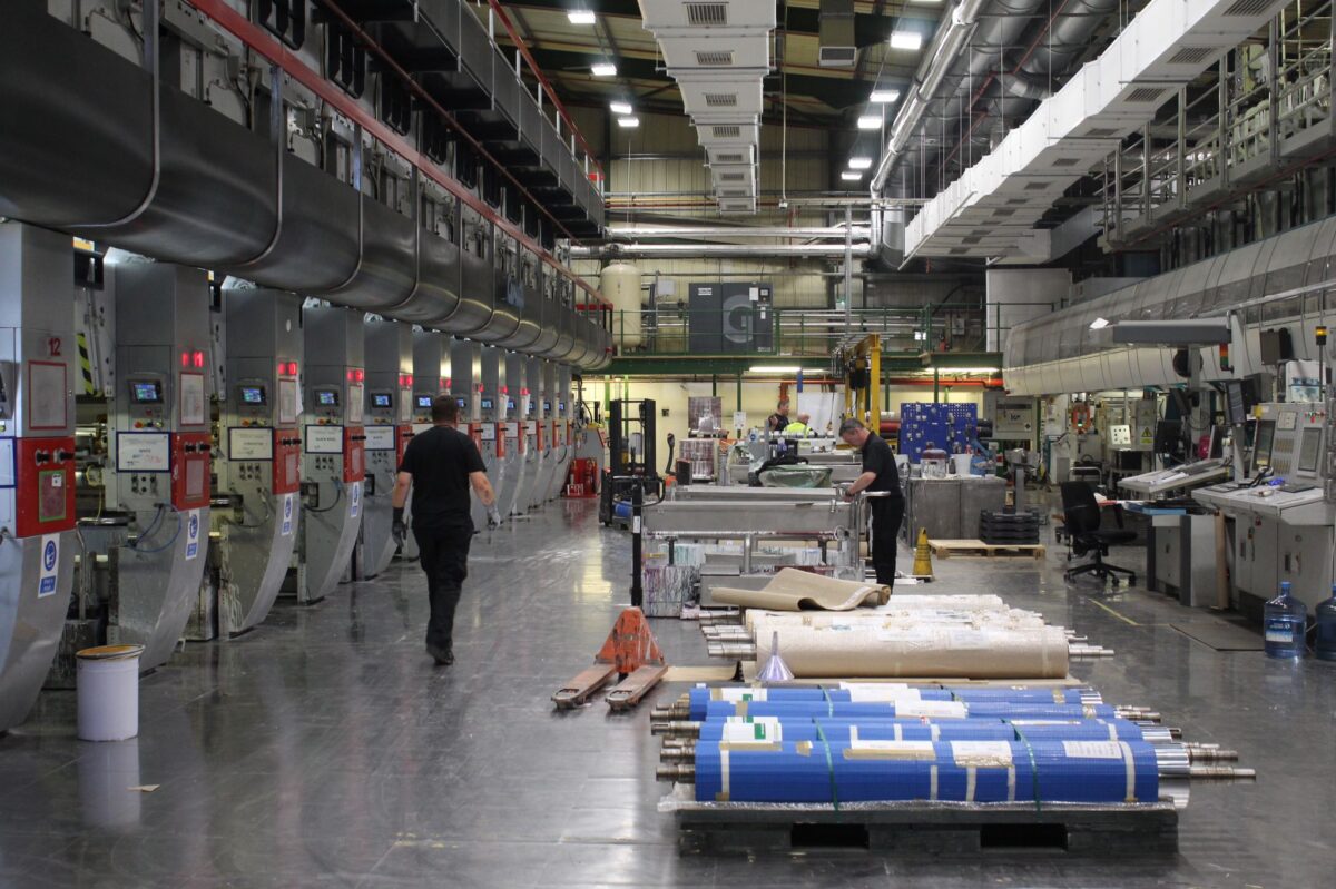 A large manufacturing work floor, with many large industrial machines and several employees.