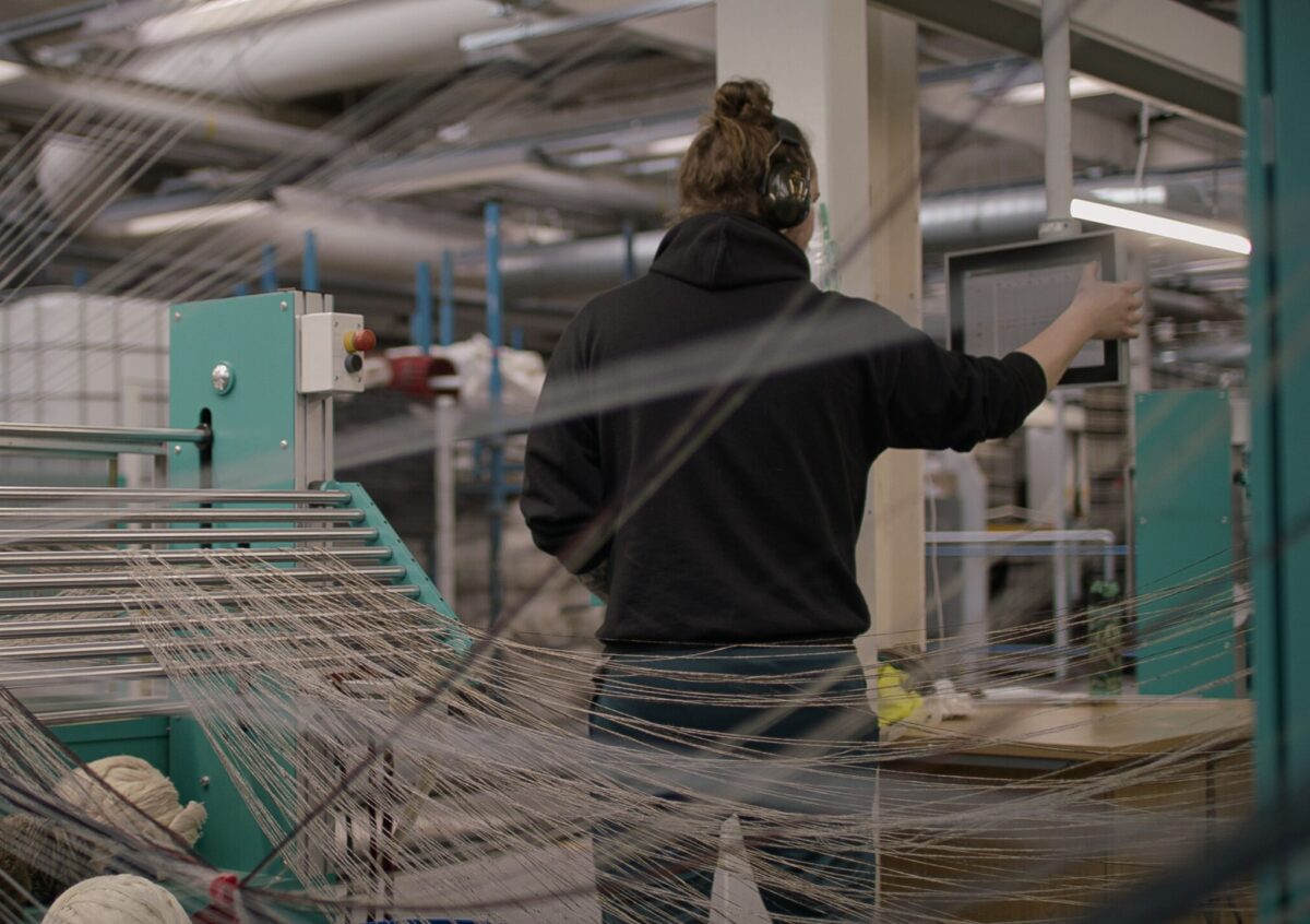 Jacob using a digital screen to interface with a weaving machine, in a textile factory.