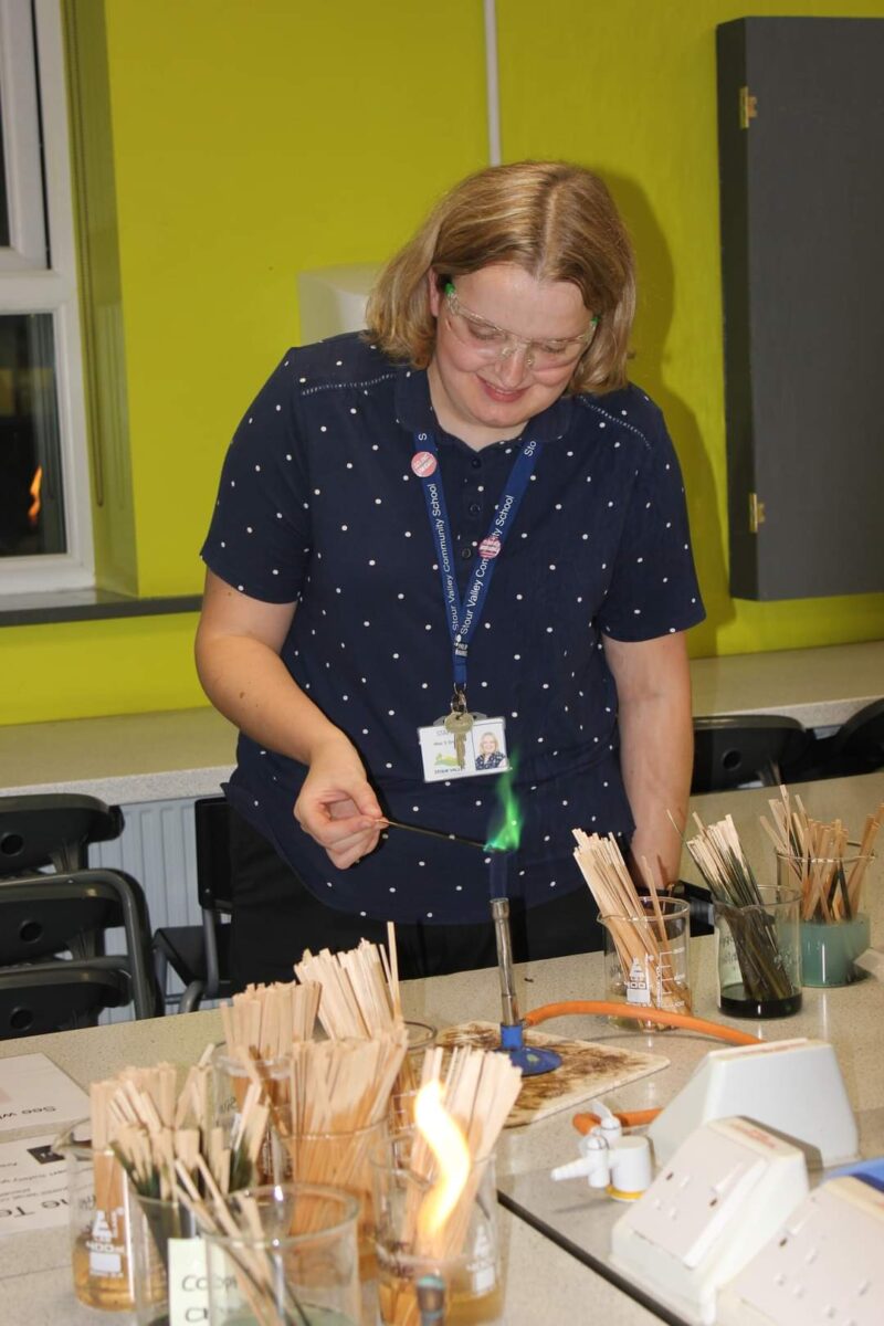 Shannon wearing protective glasses, burning a copper compound in a Bunsen burner, resulting in a green flame.