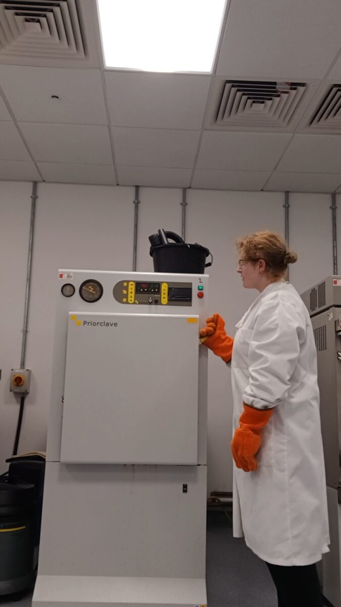River sterilising lab equipment in an autoclave, wearing a lab coat and large protective gloves.