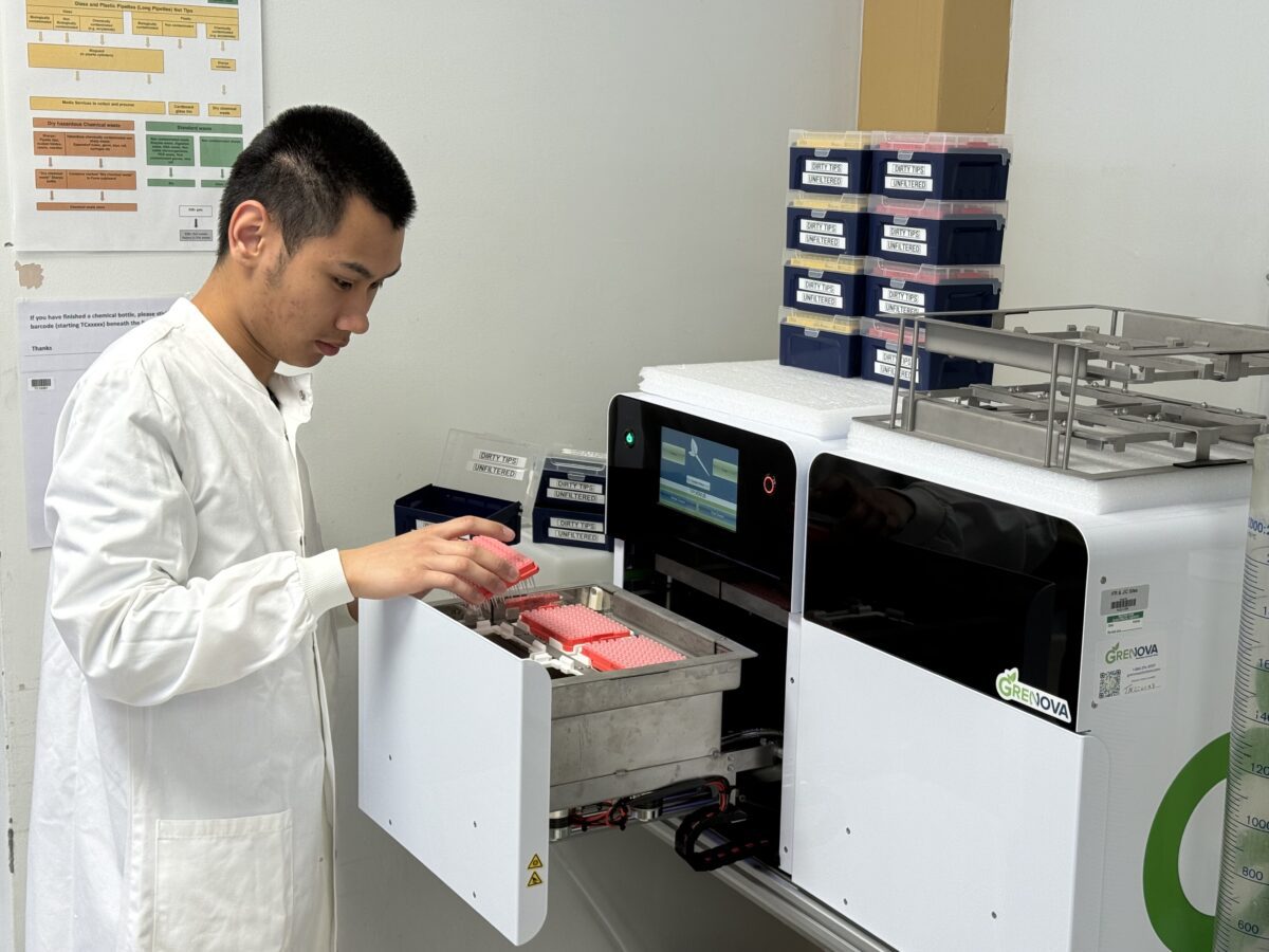 Francis wearing a lab coat, working with a piece of machinery in the lab.