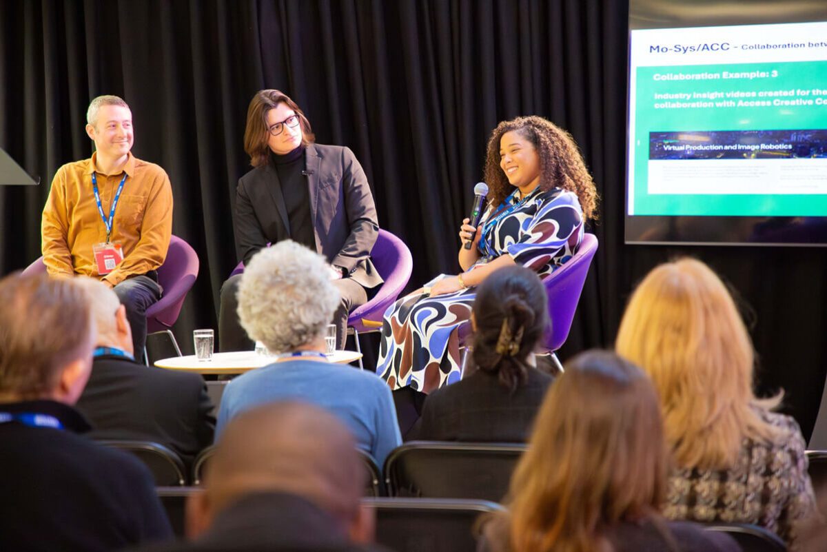 Fernanada seated on a stage with other panellists, speaking to the audience at a live event.
