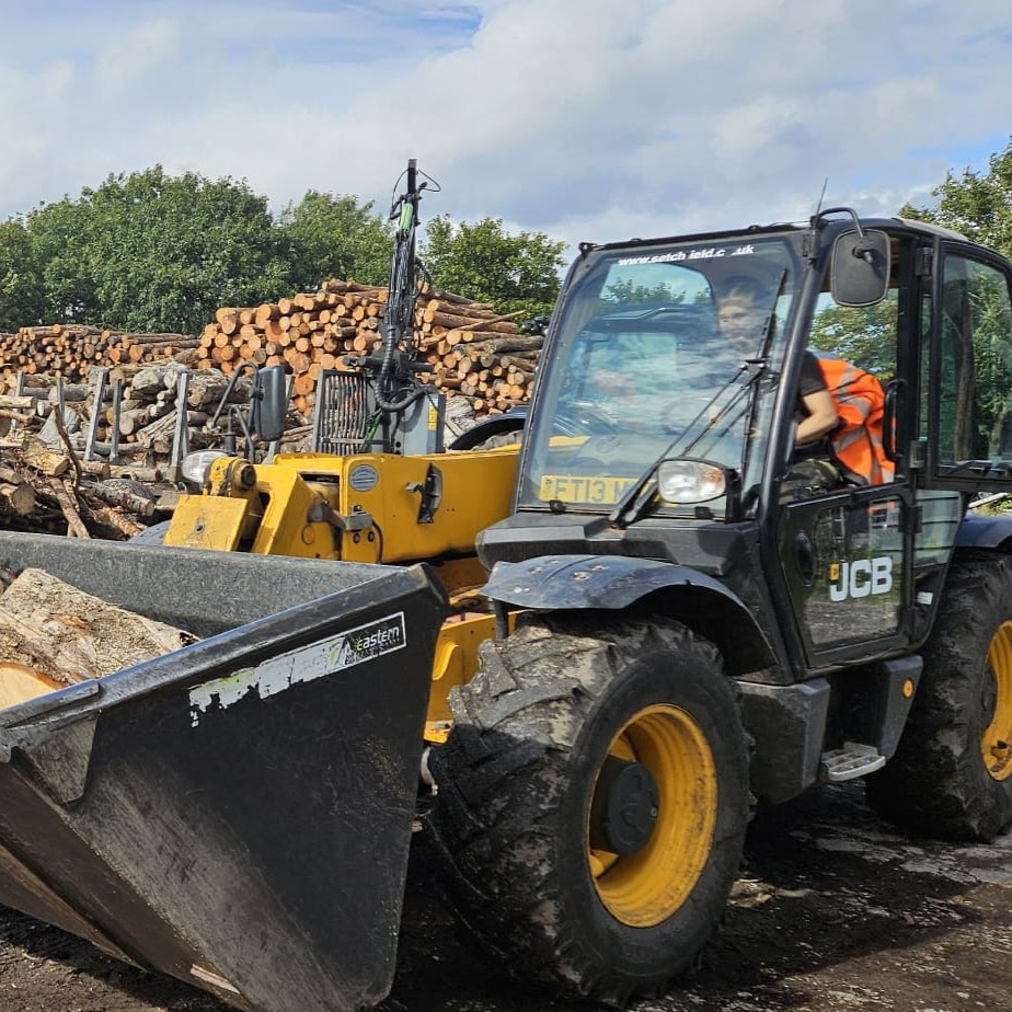 Matilda driving a JCB to move logs.