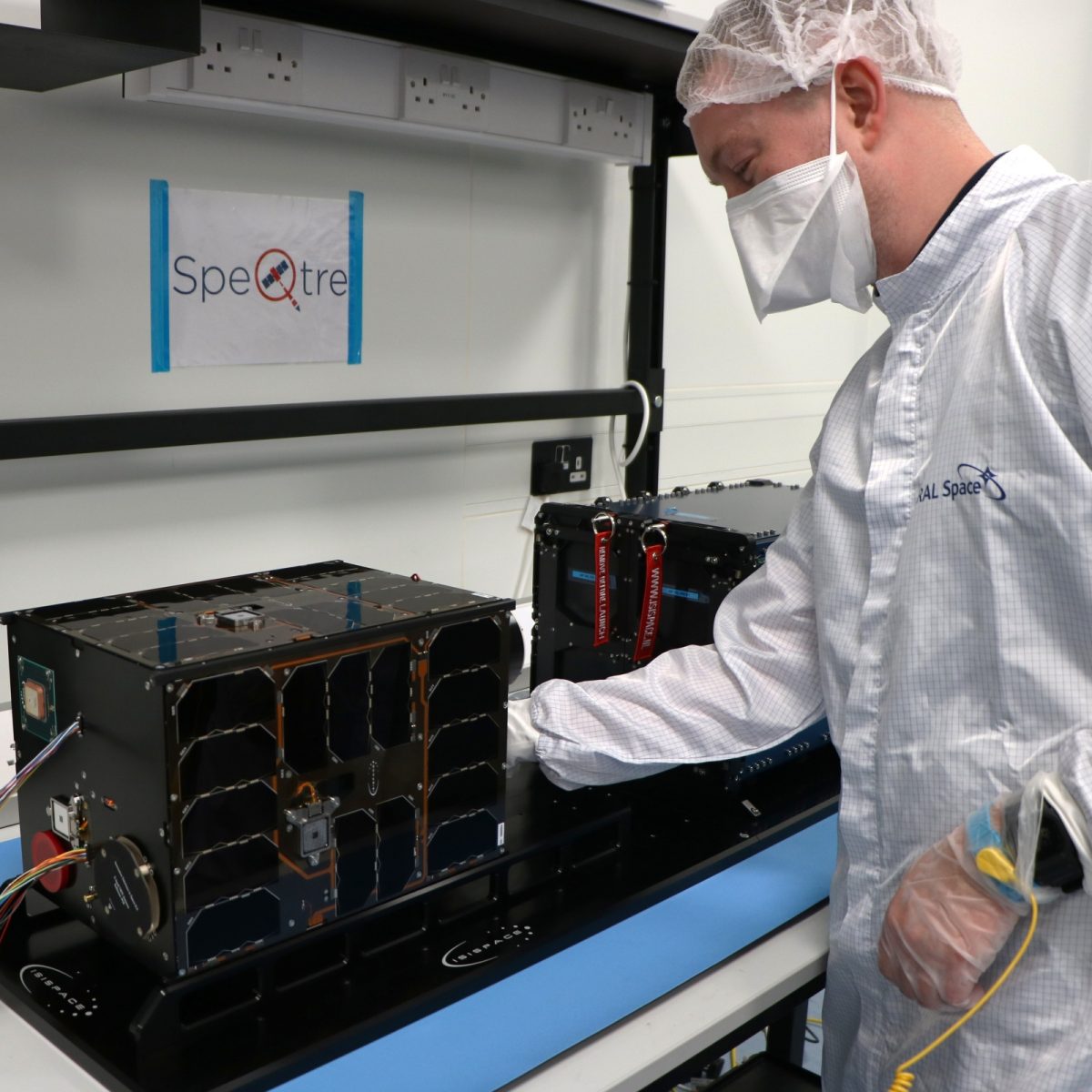 Louis wearing a full clean suit including a face mask, tinkering with a piece of equipment on a workbench.