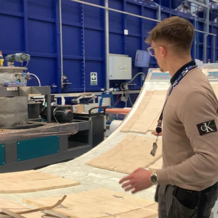 Sam on the factory floor in front of materials laid out on a large curved surface.