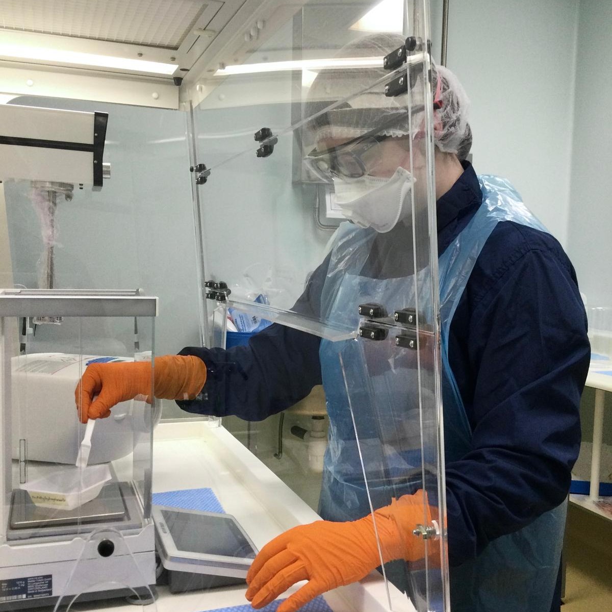 Louisa wearing an apron, facemask, hair net, safety goggles, and gloves, measuring ingredients on a weighing scales in the lab.