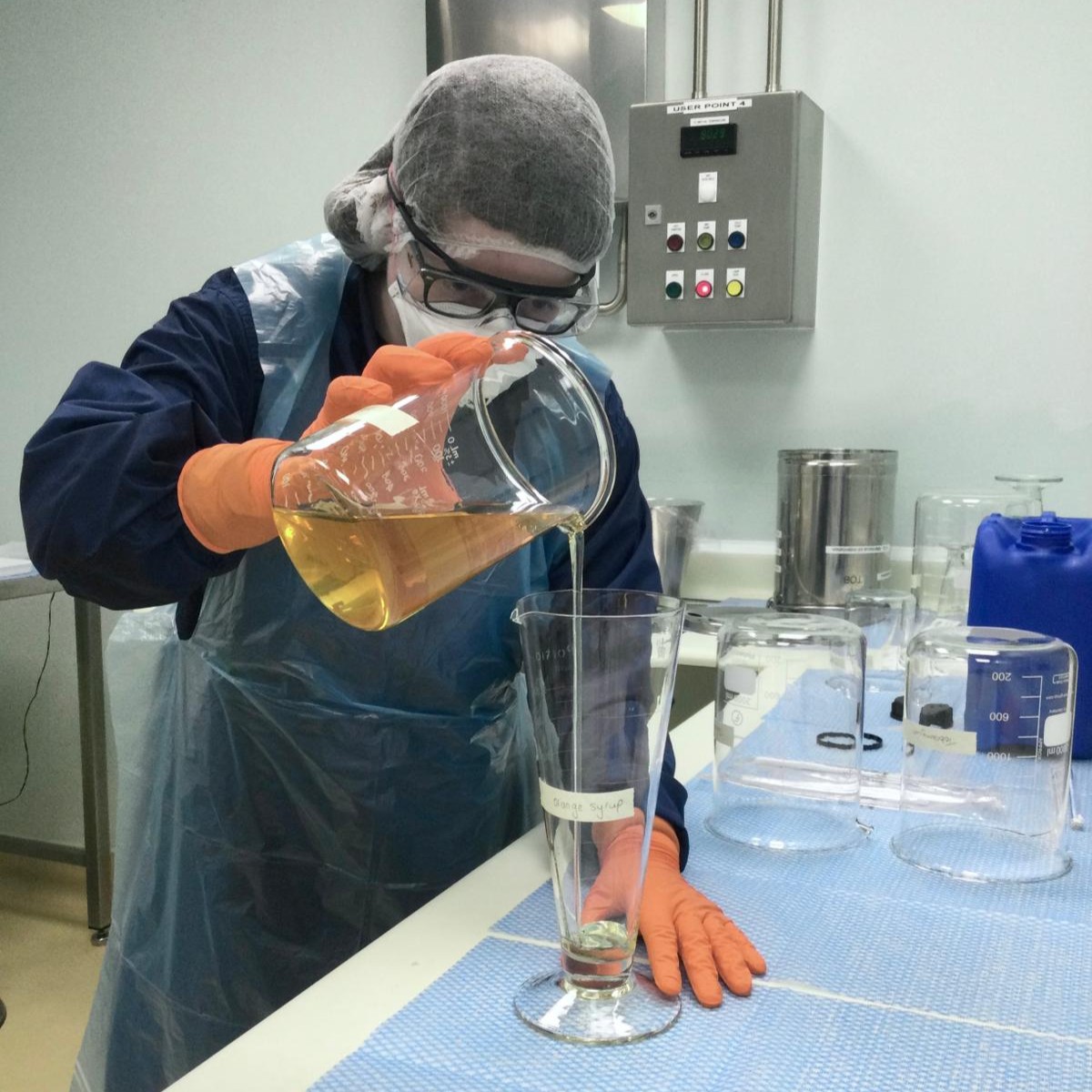 Louisa wearing an apron, facemask, safety goggles, and gloves, measuring out a liquid in the lab.
