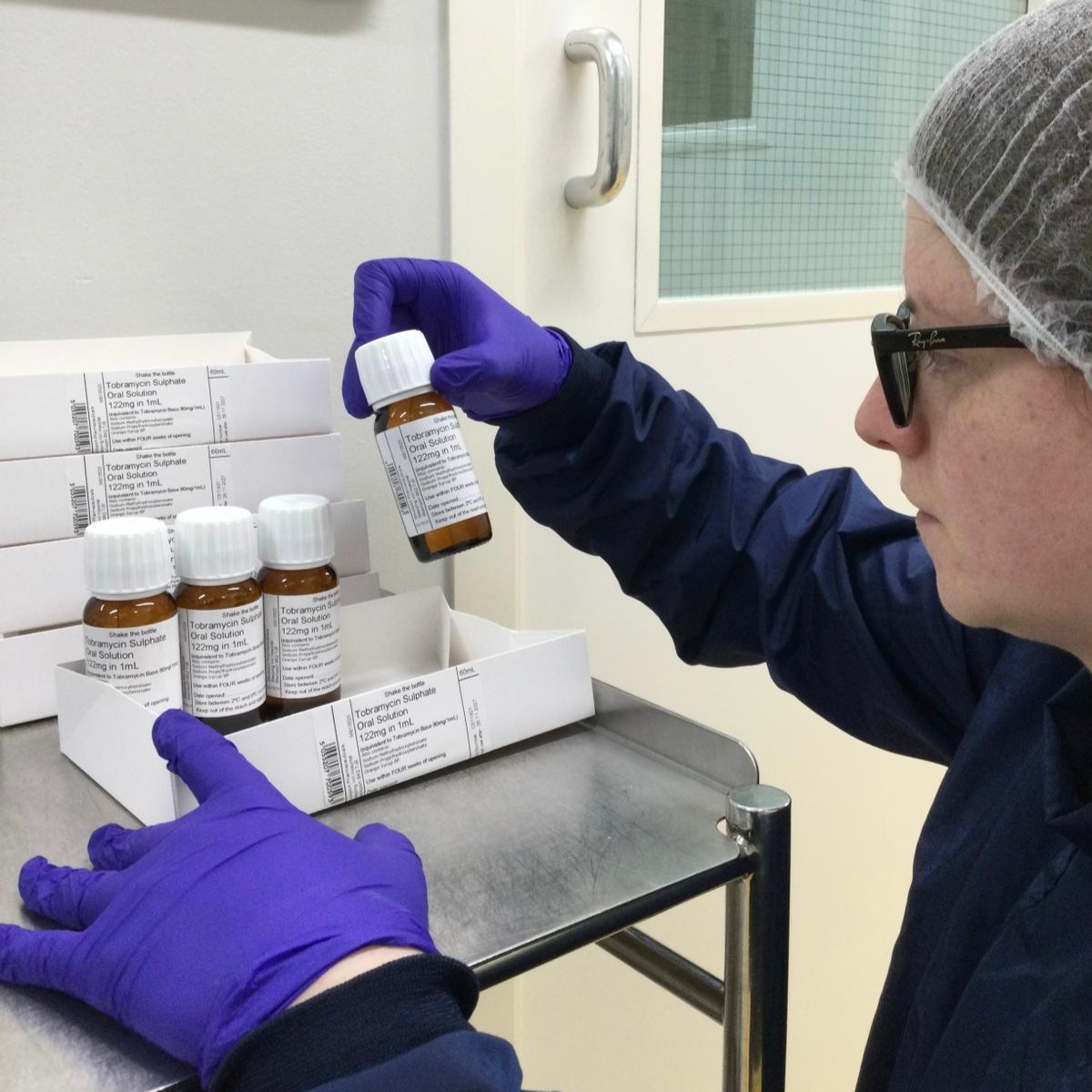 Louisa wearing a hair net and gloves, checking the labels of medicine bottles in the lab.