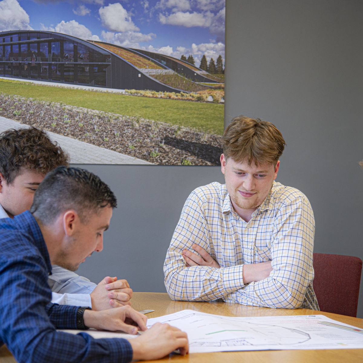 Will sat a table with two colleagues, looking at printed construction drawings.