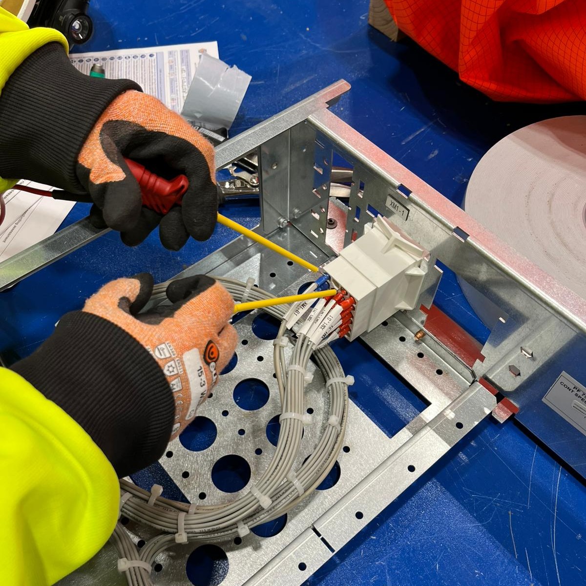 A close-up of Siwan's hands, doing electrical wiring, whilst wearing protective rubber gloves.