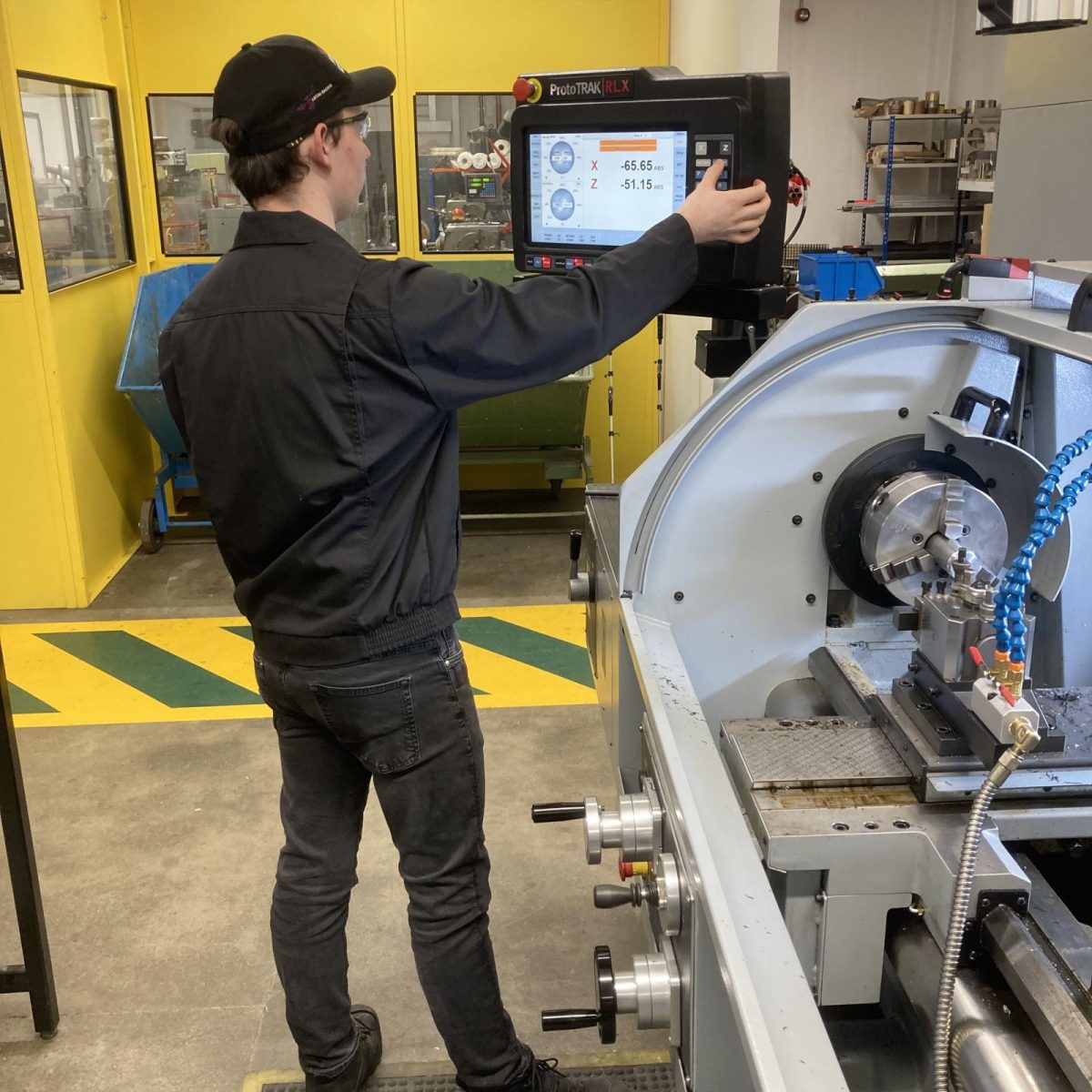 Engineering Manufacturing Technician Henry in the workshop, operating a control panel on a CNC lathe.