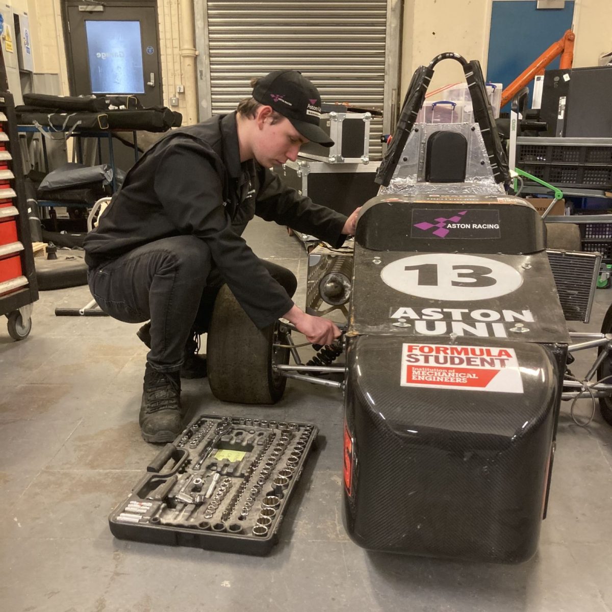 Engineering Manufacturing Technician Henry wearing overalls, kneeling on the floor to work on a racing kart.