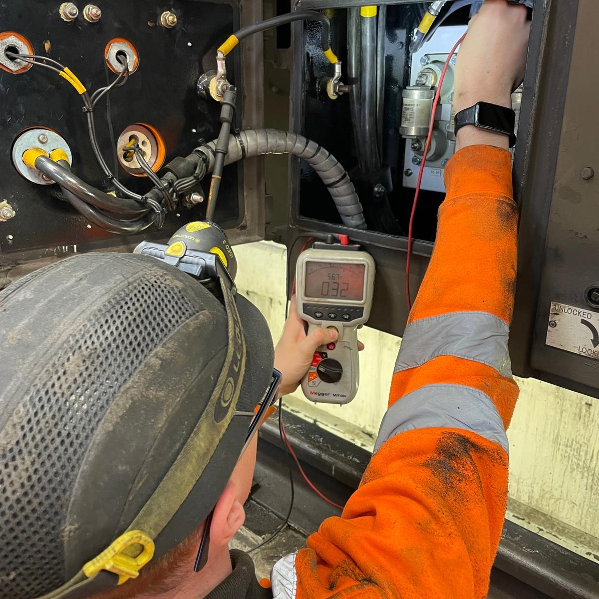 Jack, wearing overalls, gloves, safety goggles and a hard hat, using a multimeter to test an electrical system.
