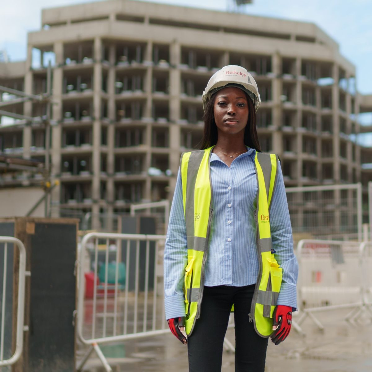 Nylah, wearing a hi-vis jacket, gloves, and hard hat, standing in a construction site.