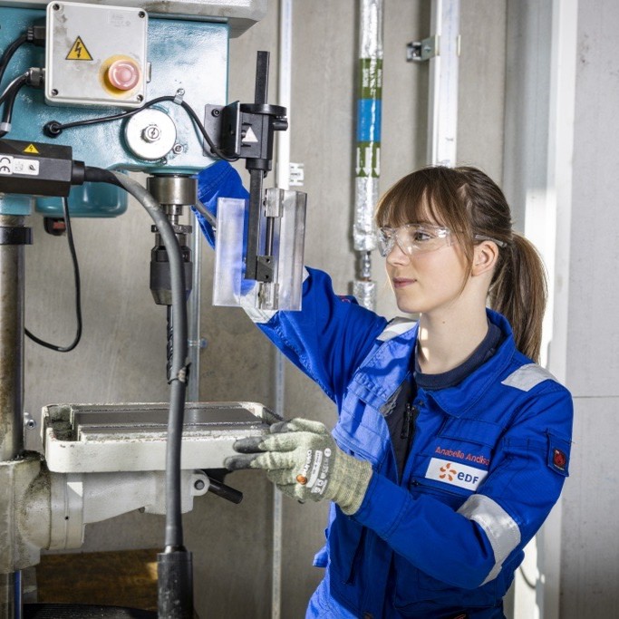 Maintenance and Operations Engineering Technician Anabella, wearing overalls, gloves and protective glasses, using a drill press.