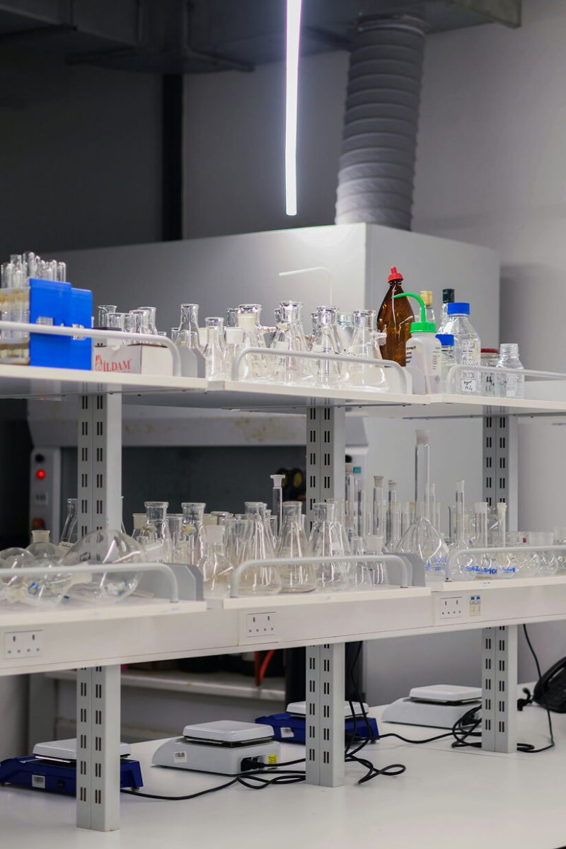 Shelves in a lab lined up with various glass lab equipment like conical flasks