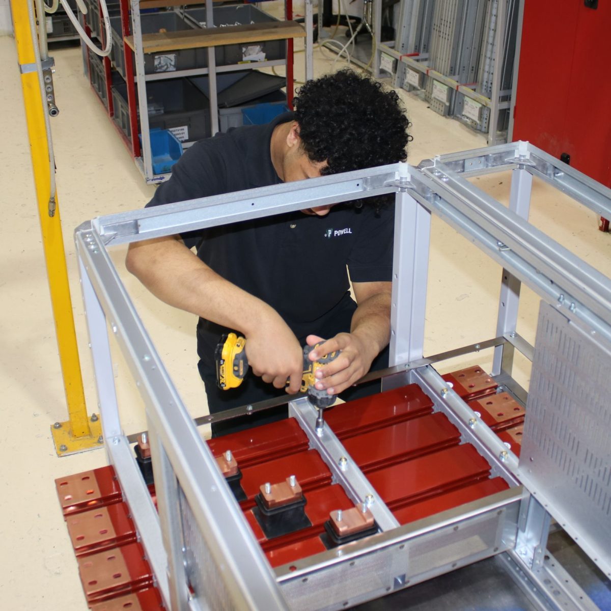 Electrical Engineering Technician Micah, on the workshop floor, using a tool to put a new electrical cabinet together.
