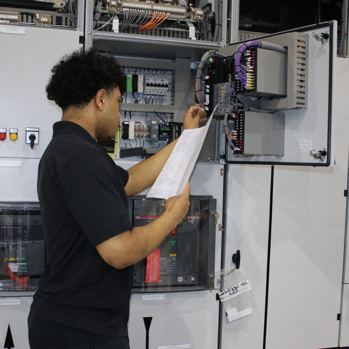 Electrical Engineering Technician Micah, following a wiring diagram to wire up a cabinet full of electrical components, on the workshop floor.