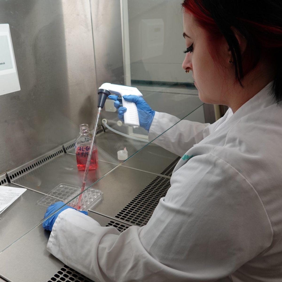 Research Laboratory Technician Oliwia in the lab, wearing a lab coat and gloves, measuring chemicals in a fume cupboard.