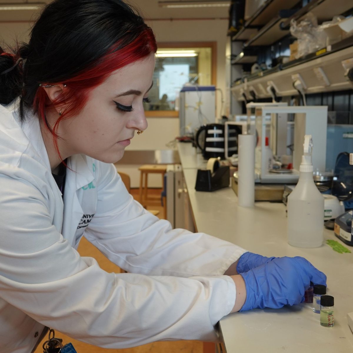 Research Laboratory Technician Oliwia in the lab, wearing a lab coat and gloves, handling some tiny vials.