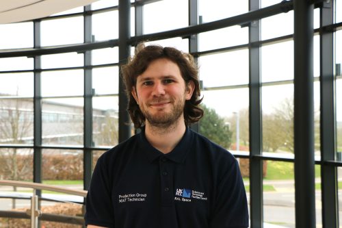 A man stood in the centre smiling at the camera wearing a work branded polo t-shirt