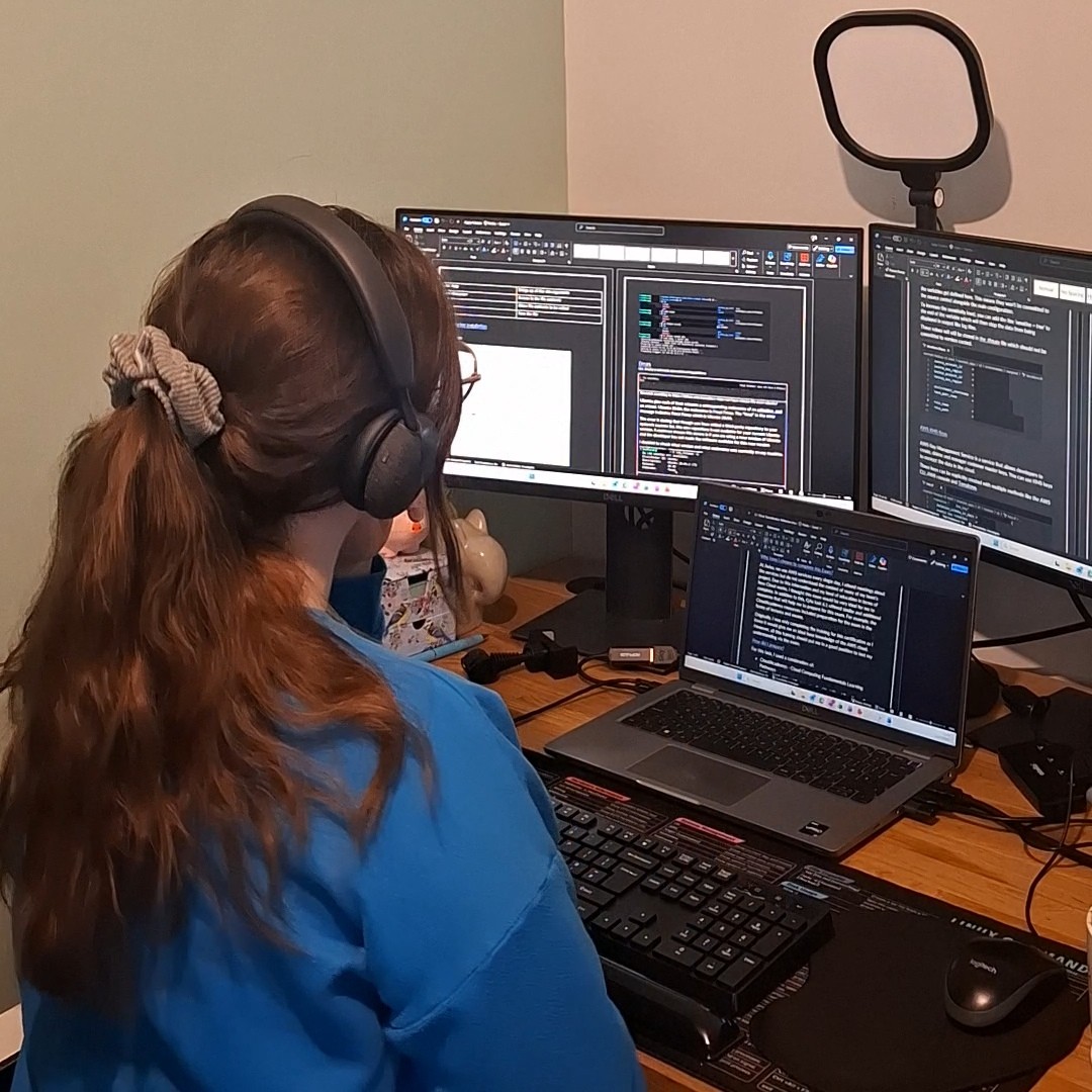 Software Developer Ria wearing headphones, working at her desk with her laptop and two additional screens.