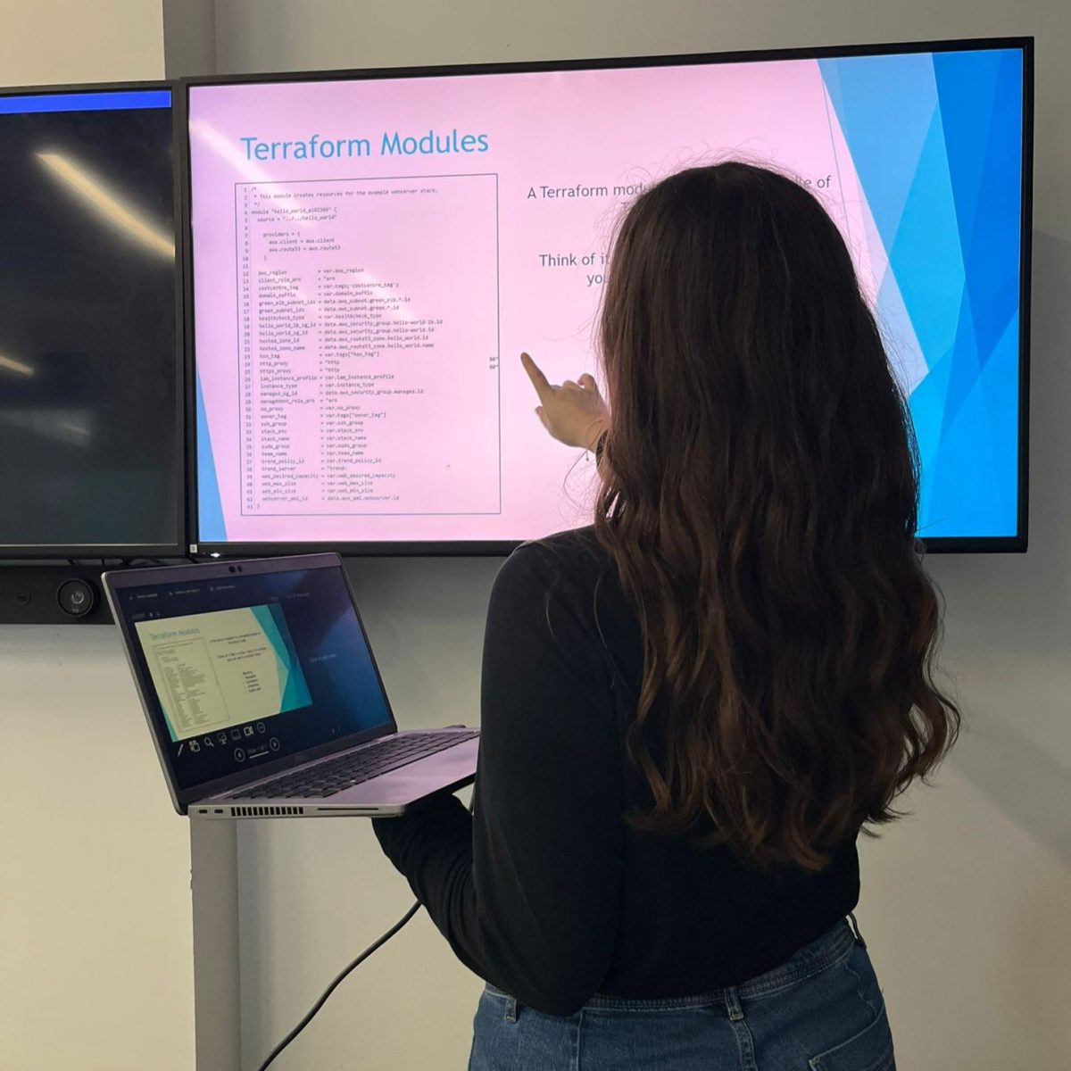 Software Developer Ria, in the middle of a presentation, pointing at a large screen on the wall, which is connected to her laptop.